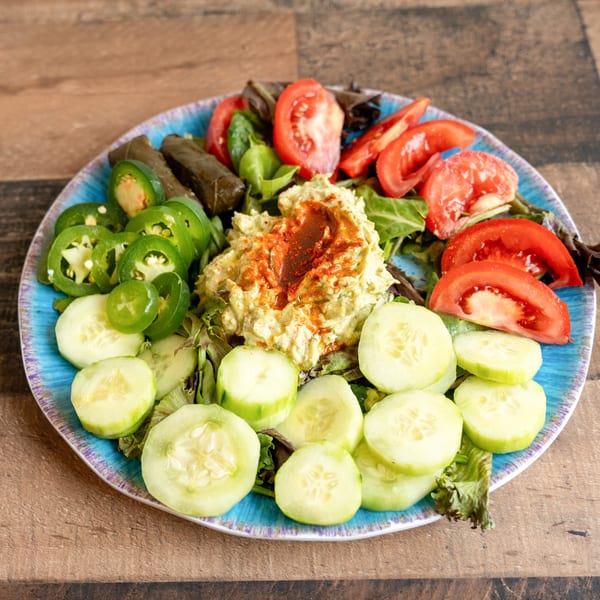 Colorful Mediterranean platter with hummus, tomatoes, cucumbers, jalapeños, and stuffed grape leaves.