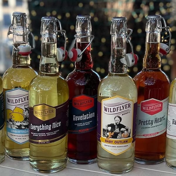 A variety of Wildflyer Mead bottles with colorful labels are displayed on a wooden surface.