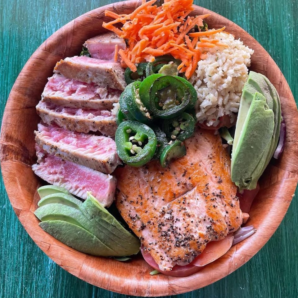 Seared tuna, salmon, avocado, jalapeños, carrots, and brown rice in a wooden bowl.