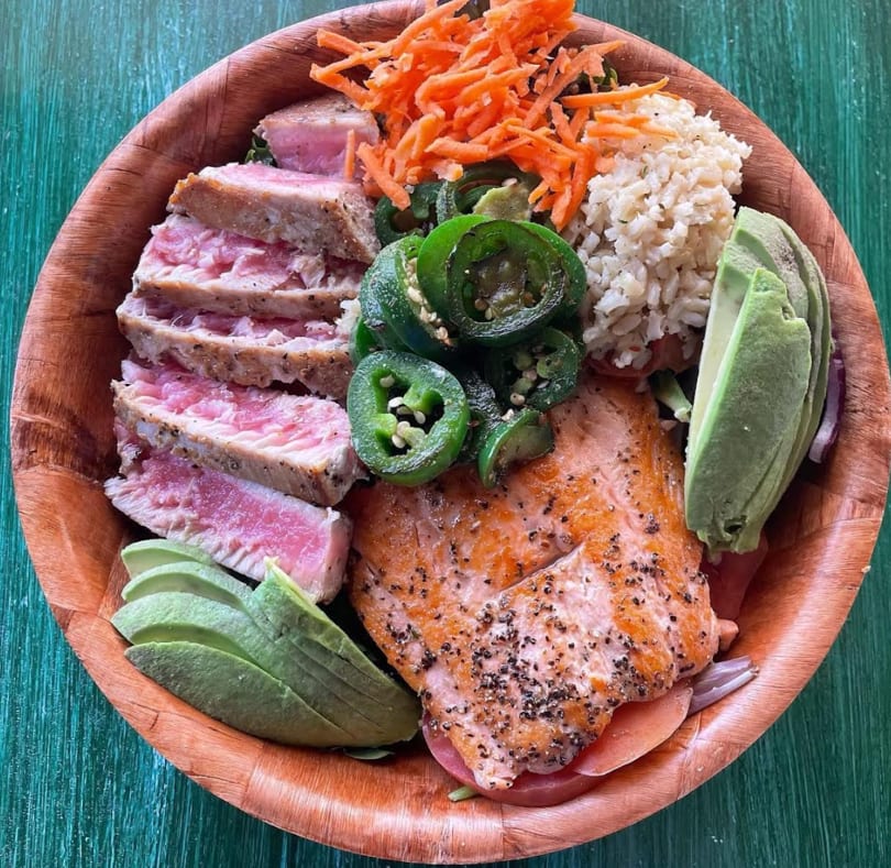 Seared tuna, salmon, avocado, jalapeños, carrots, and brown rice in a wooden bowl.