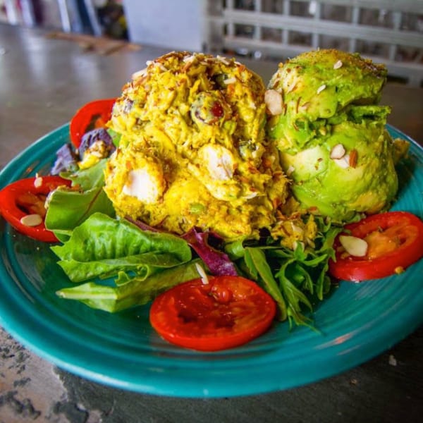 Curry chicken salad and avocado salad with lettuce, tomatoes, and almonds on a teal plate.