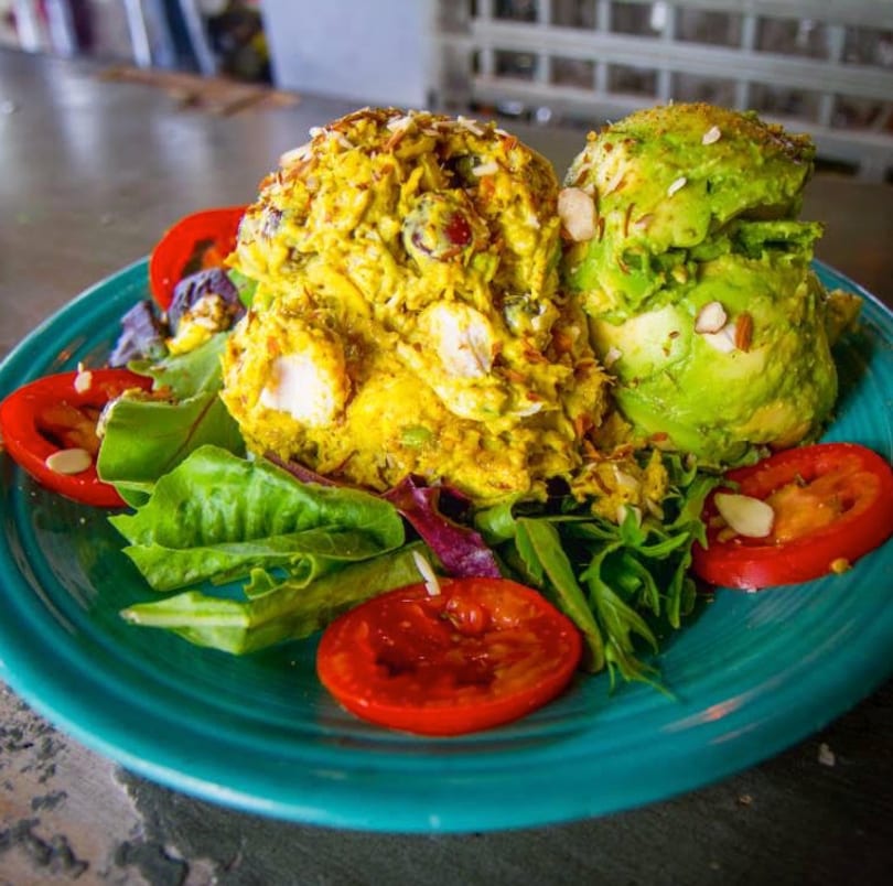 Curry chicken salad and avocado salad with lettuce, tomatoes, and almonds on a teal plate.