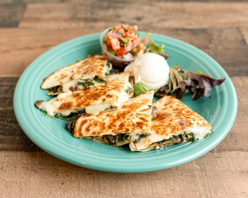 Mushroom and spinach quesadillas with melted cheese, served with salsa, sour cream, and greens.