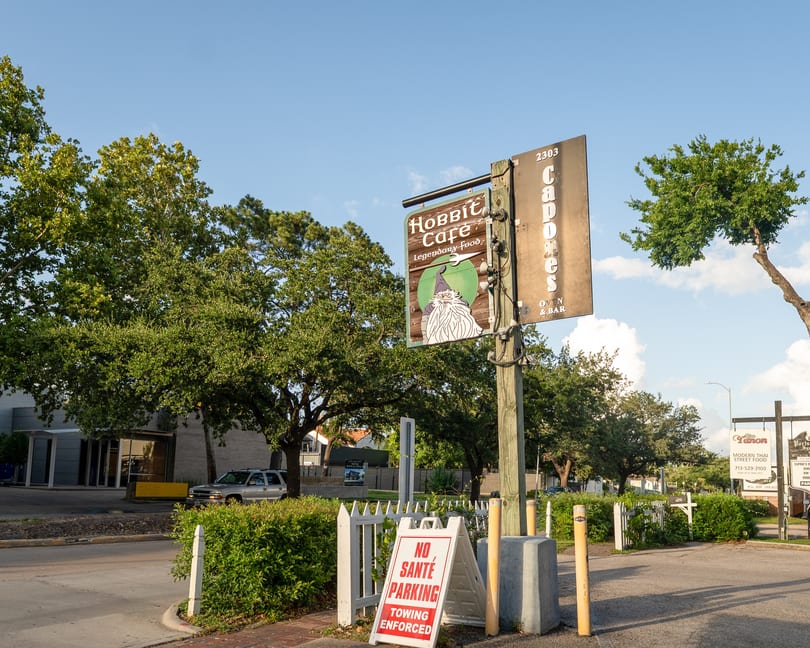 A street view of the Hobbit Cafe sign, with a wizard illustration, and a "No Parking" sign.
