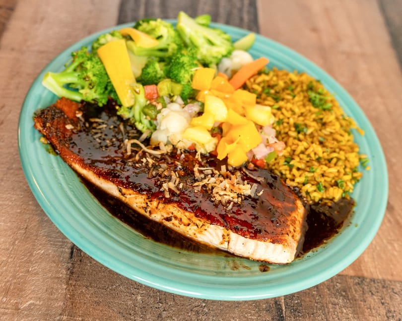 Teriyaki salmon with rice, broccoli, and mixed vegetables on a teal plate.