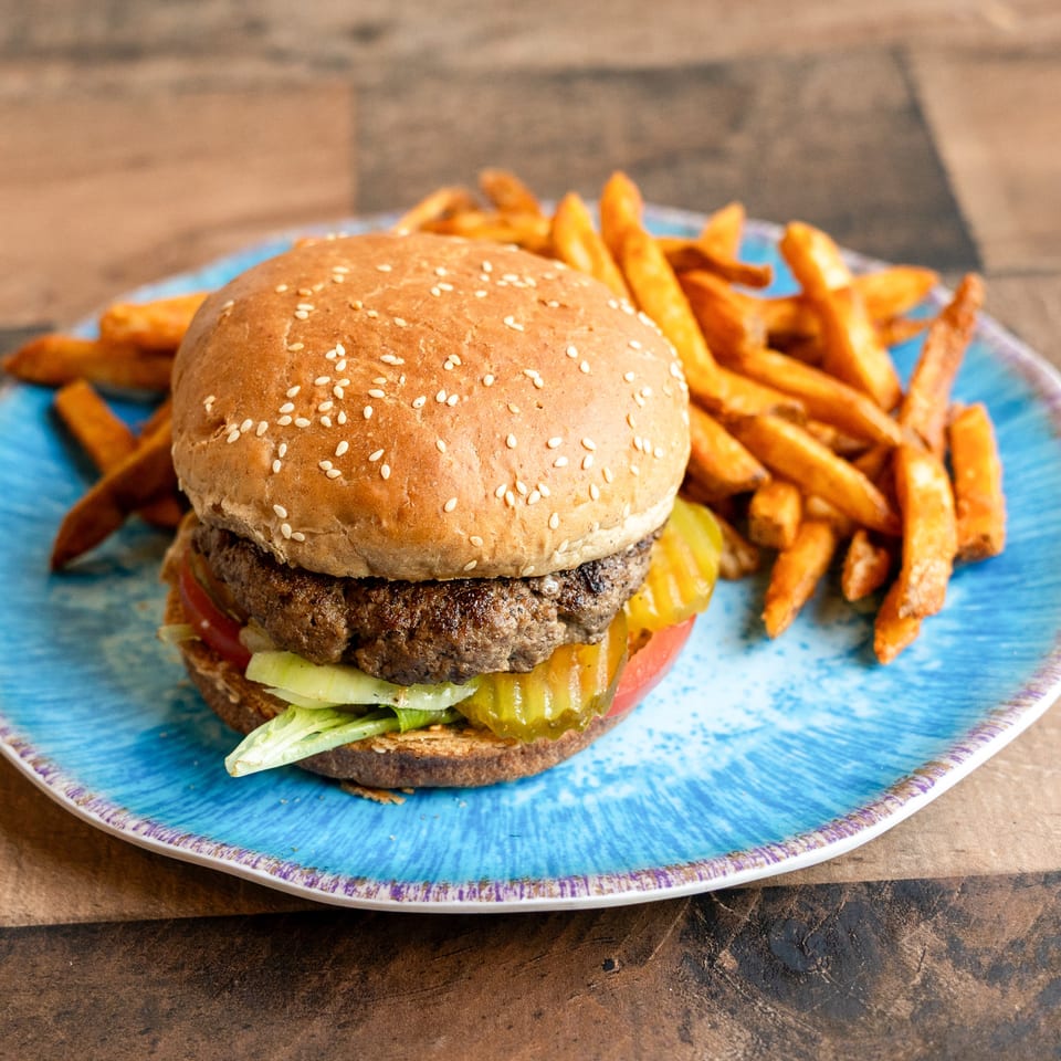 A juicy burger with lettuce, tomato, and pickles, served with a side of fries on a blue plate.