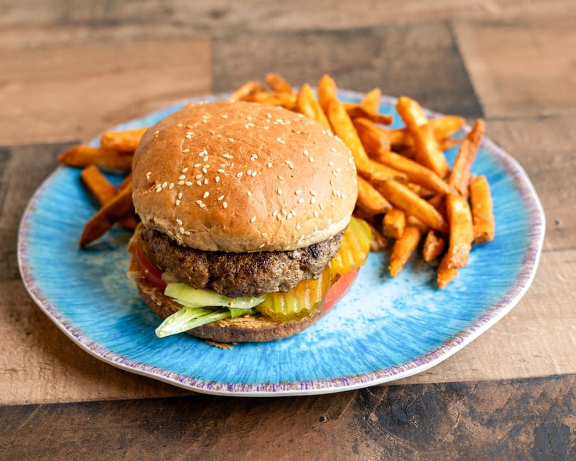 A juicy burger with lettuce, tomato, and pickles, served with a side of fries on a blue plate.