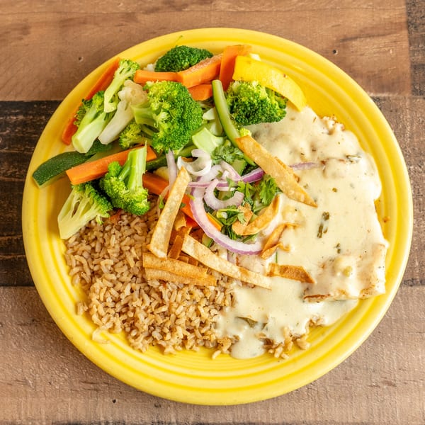A yellow plate holds a meal with rice, chicken in cream sauce, and steamed vegetables.