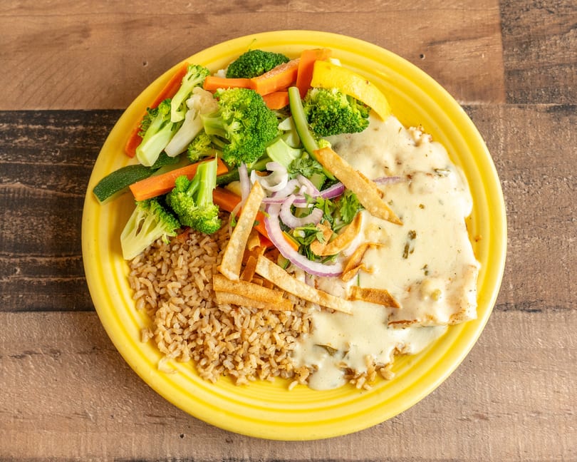 A yellow plate holds a meal with rice, chicken in cream sauce, and steamed vegetables.