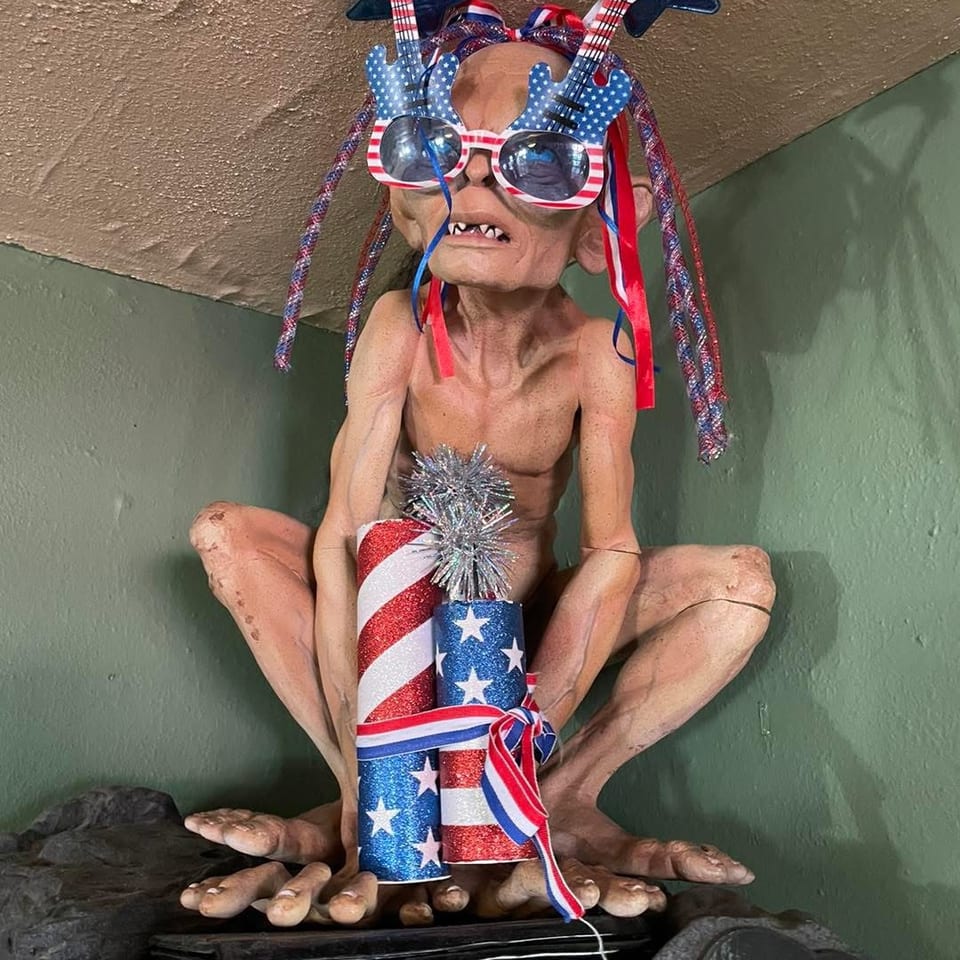 Gollum figurine wearing patriotic guitar glasses and holding red, white, and blue firecrackers.