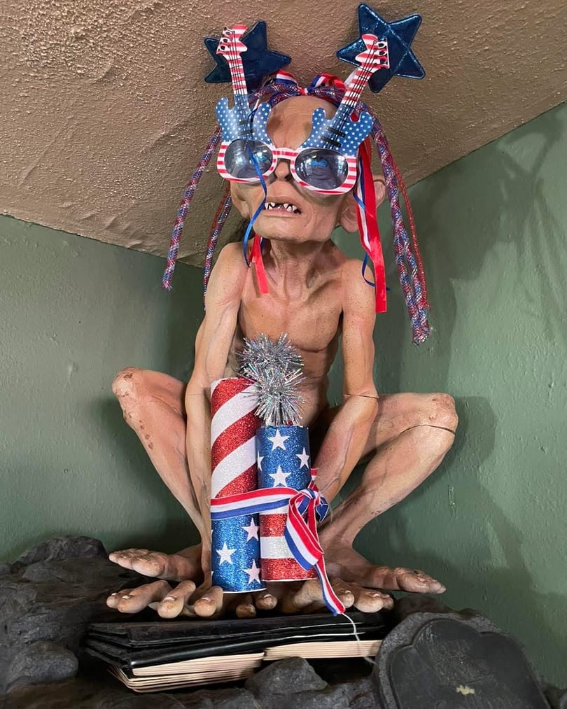 Gollum figurine wearing patriotic guitar glasses and holding red, white, and blue firecrackers.