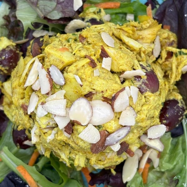 Curry chicken salad with grapes and sliced almonds, served on a bed of mixed greens.