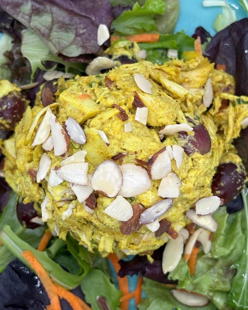 Curry chicken salad with grapes and sliced almonds, served on a bed of mixed greens.