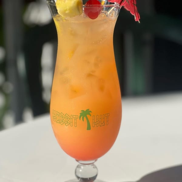 A vibrant orange and red cocktail with pineapple, cherry, and a red umbrella, on a white table.