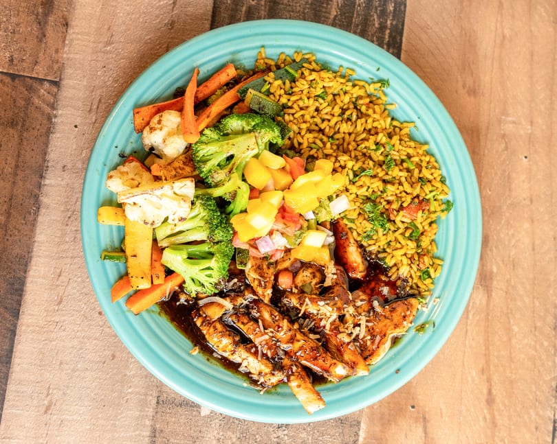 A vibrant plate of jerk chicken, yellow rice, roasted vegetables, and mango salsa.