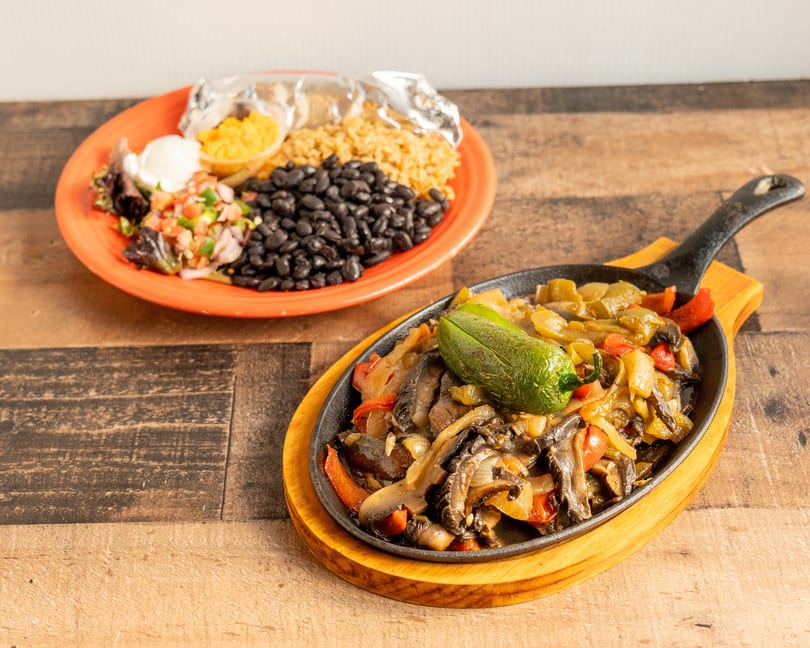 Sizzling fajitas with bell peppers, onions, and mushrooms, served with a side of rice and black beans.