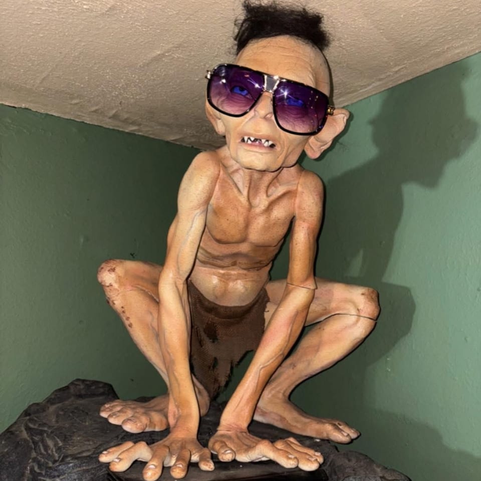 Gollum figurine from Lord of the Rings wearing sunglasses and a small wig, crouching on a book.