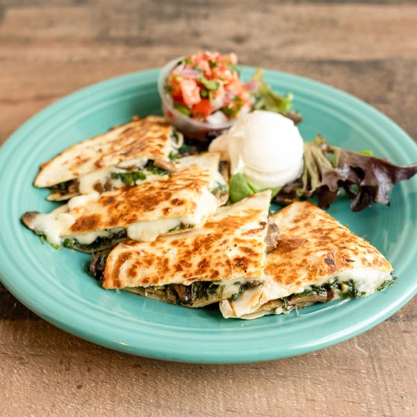 Four quesadilla slices filled with cheese and spinach, served with salsa, sour cream, and lettuce.
