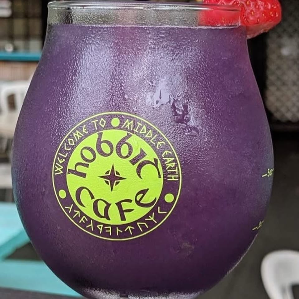 Purple drink with a strawberry garnish and a "Hobbit Cafe" logo on the glass.