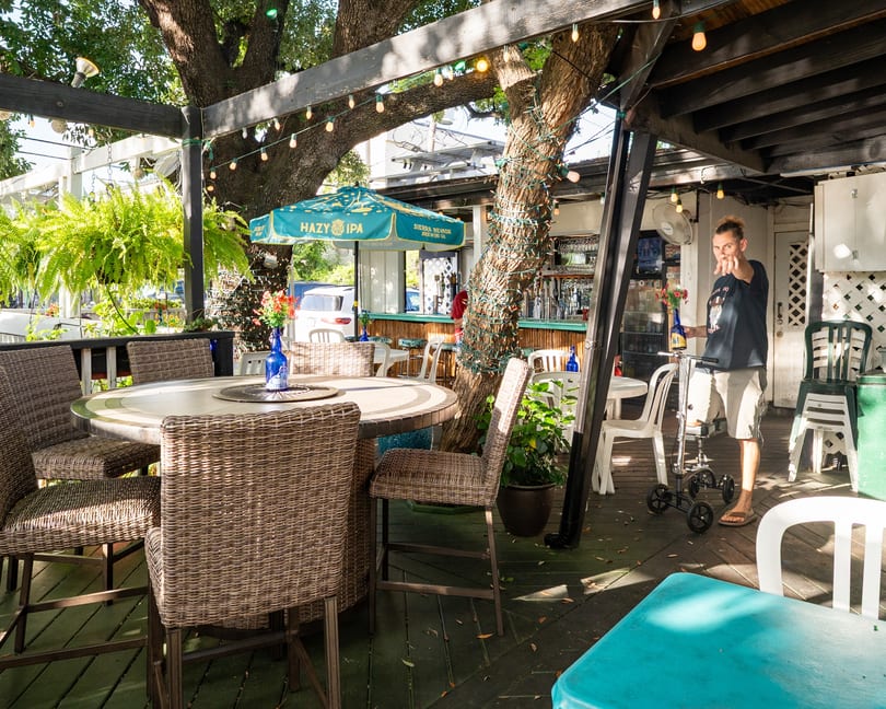 An outdoor patio with wicker chairs, a round table, string lights, and a person pointing.